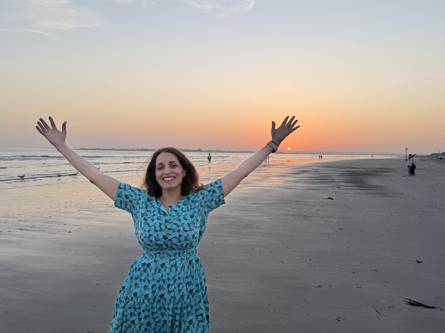 Bushra with her arms raised, laughing, on the beach at sunset
